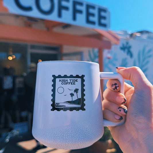white coffee mug with a graphic resembling a stamp that says high tide coffee