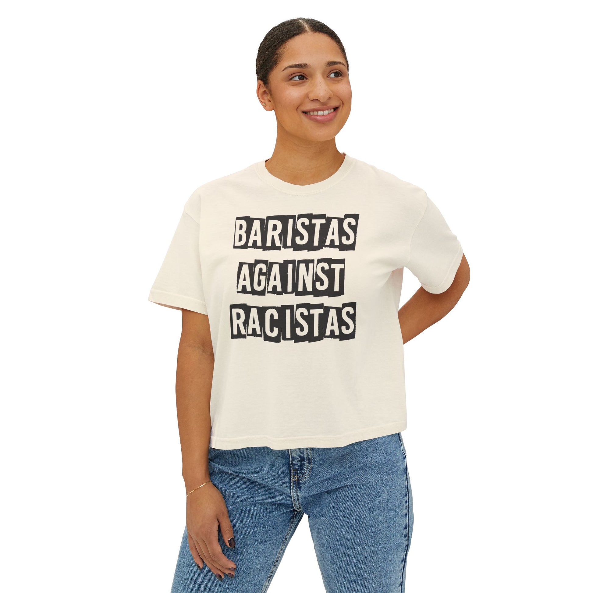A young lady standing, wearing a cream colored tee shirt that says Baristas Against Racistas