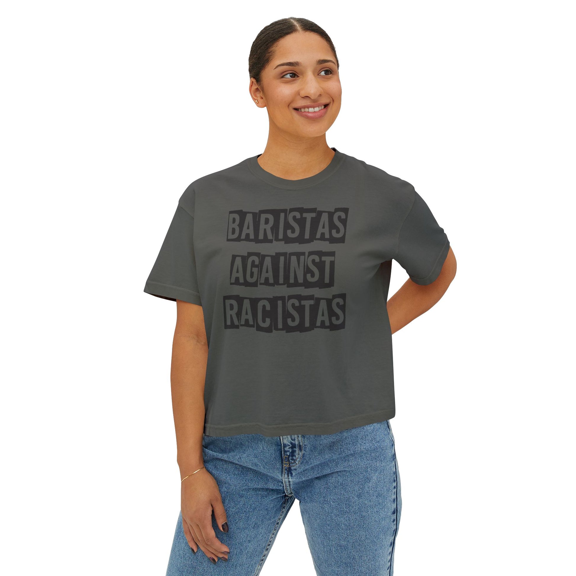 A young lady standing, wearing a dark gray tee shirt that says Baristas Against Racistas