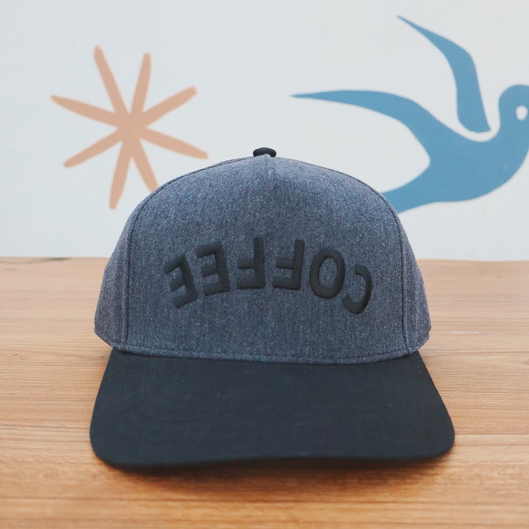 Gray cap with 'COFFEE' text on a wooden surface with abstract designs in the background
