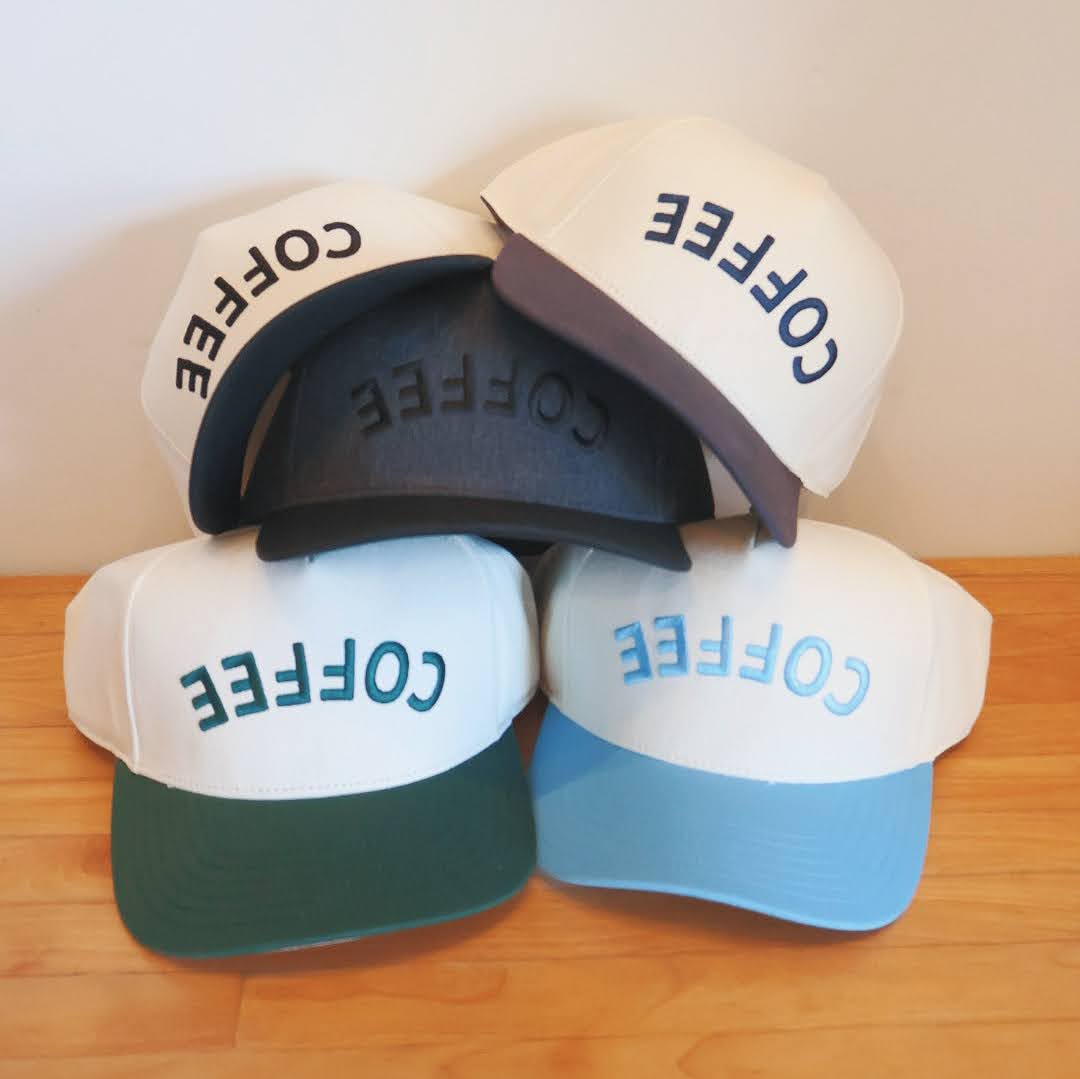 Four baseball caps with 'COFFEE' text on a wooden surface