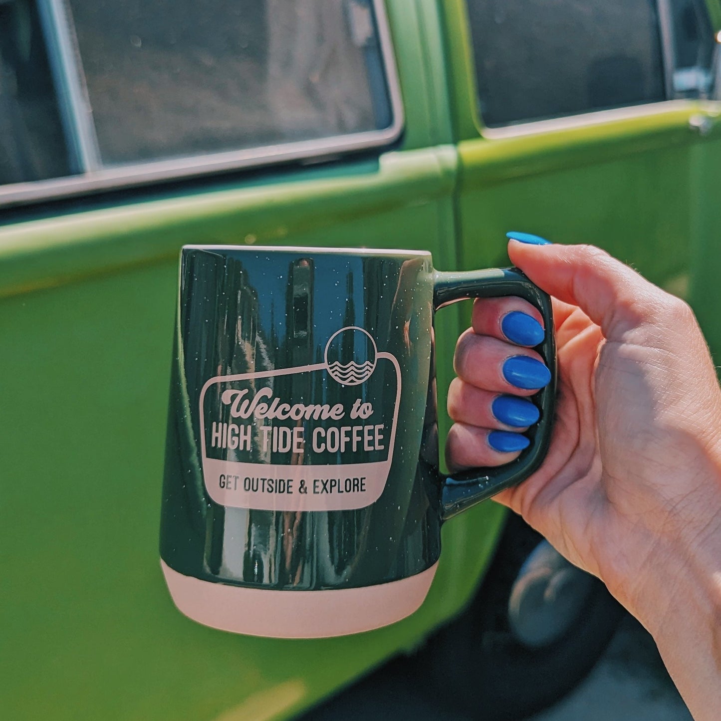 hand holding a Green Mug with Welcome to High Tide Coffee printed on it